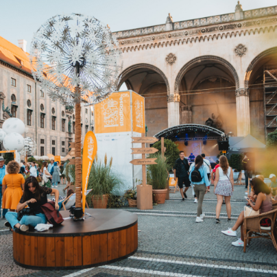 Stadtoase auf dem Odeonsplatz mit Löwenbrunnen, Pusteblumen-Skulptur, Infosäule und Besucher:innen vor der Feldherrnhalle